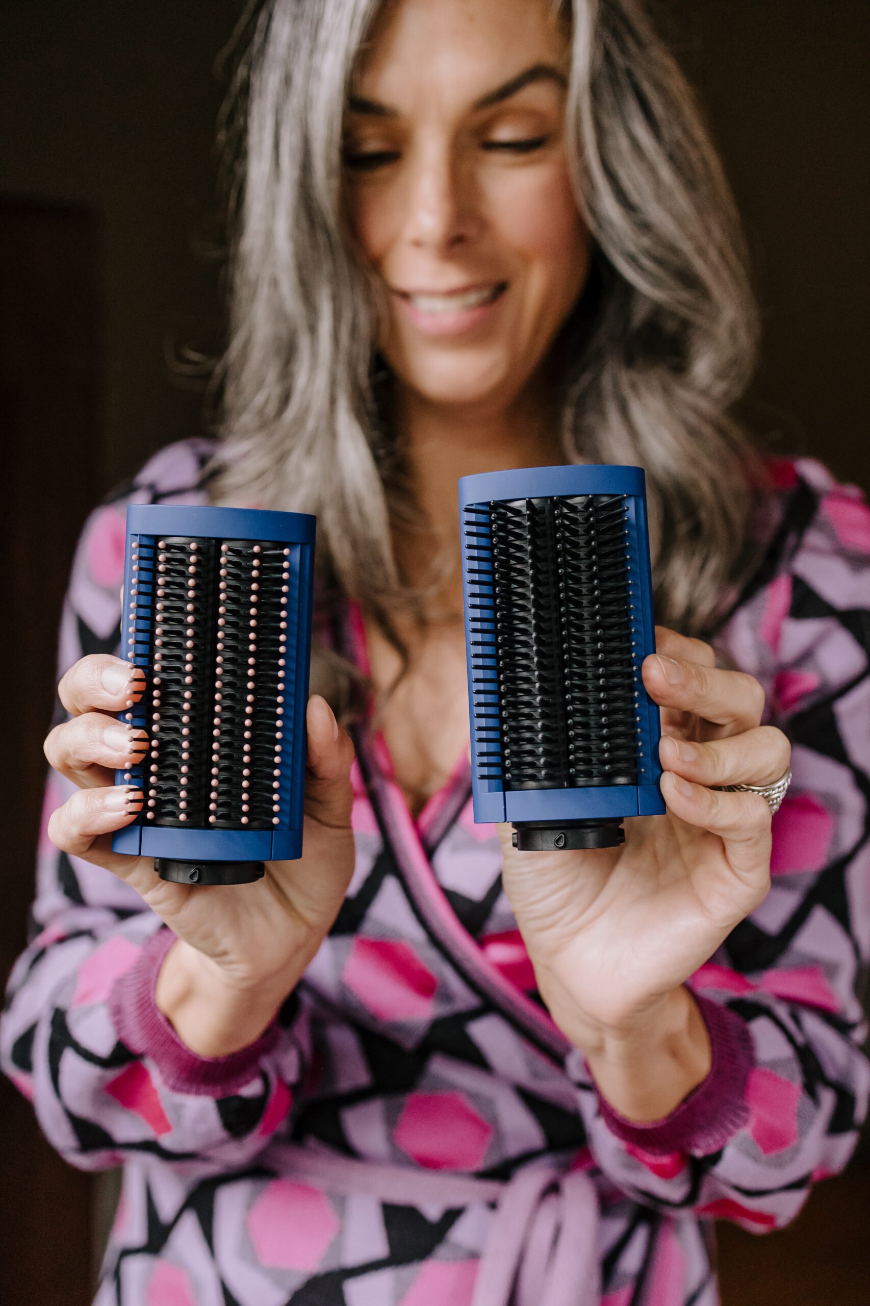 A woman with long gray hair holds up the Dyson Airwrap smoothing brushes.