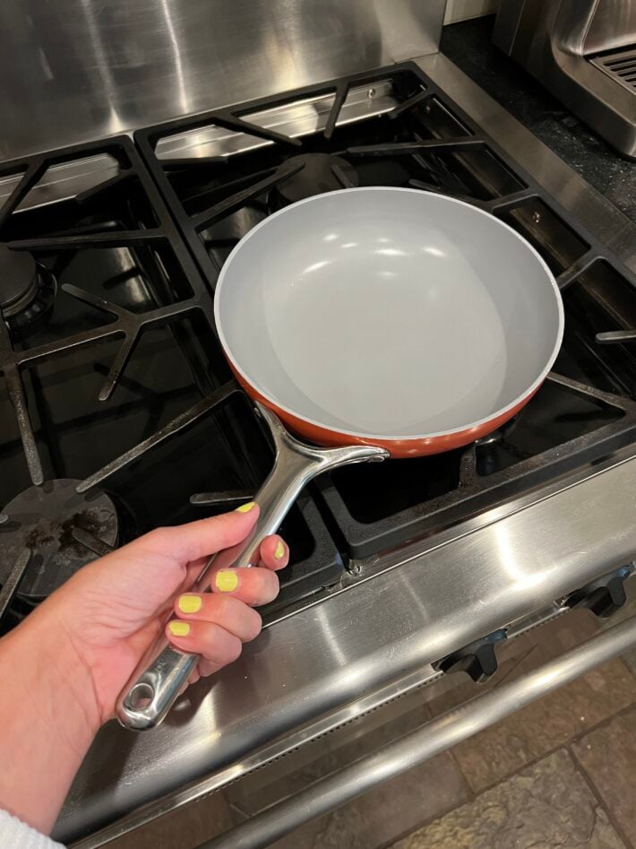 A Caraway Fry Pan sits on a gas range.