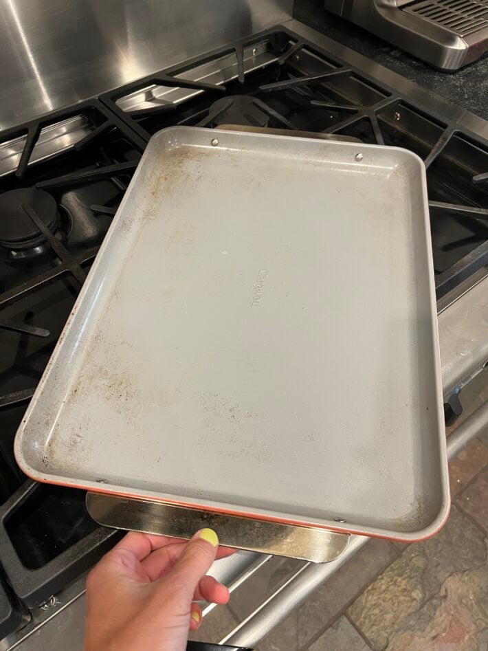 A Caraway Baking Sheet sits on a gas range.