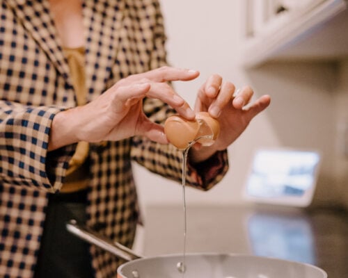A woman cracks a egg into a pan.