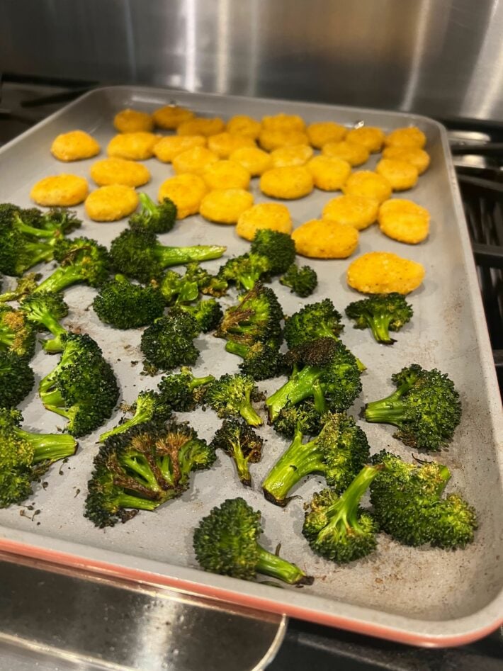 Roasted broccoli and chicken nuggets on a large baking sheet from Caraway.