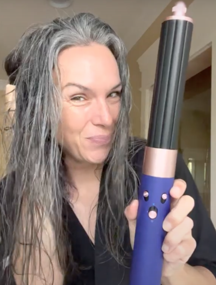 A woman uses the Dyson Airwrap to style her long gray hair.