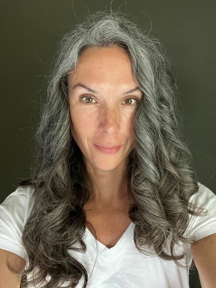 A woman with long curly gray hair immediately after using the Dyson Airwrap 1.2 inch long barrel.