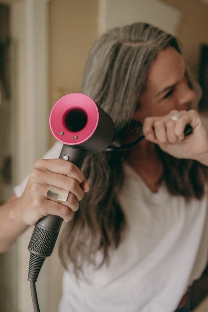 Woman blow dries her long gray hair with Dyson Supersonic Hair Dryer. 