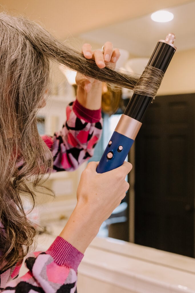 Woman styles her long gray hair with Dyson Airwrap.