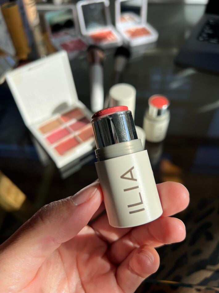 A hand holds up ILIA's multi-stick makeup.