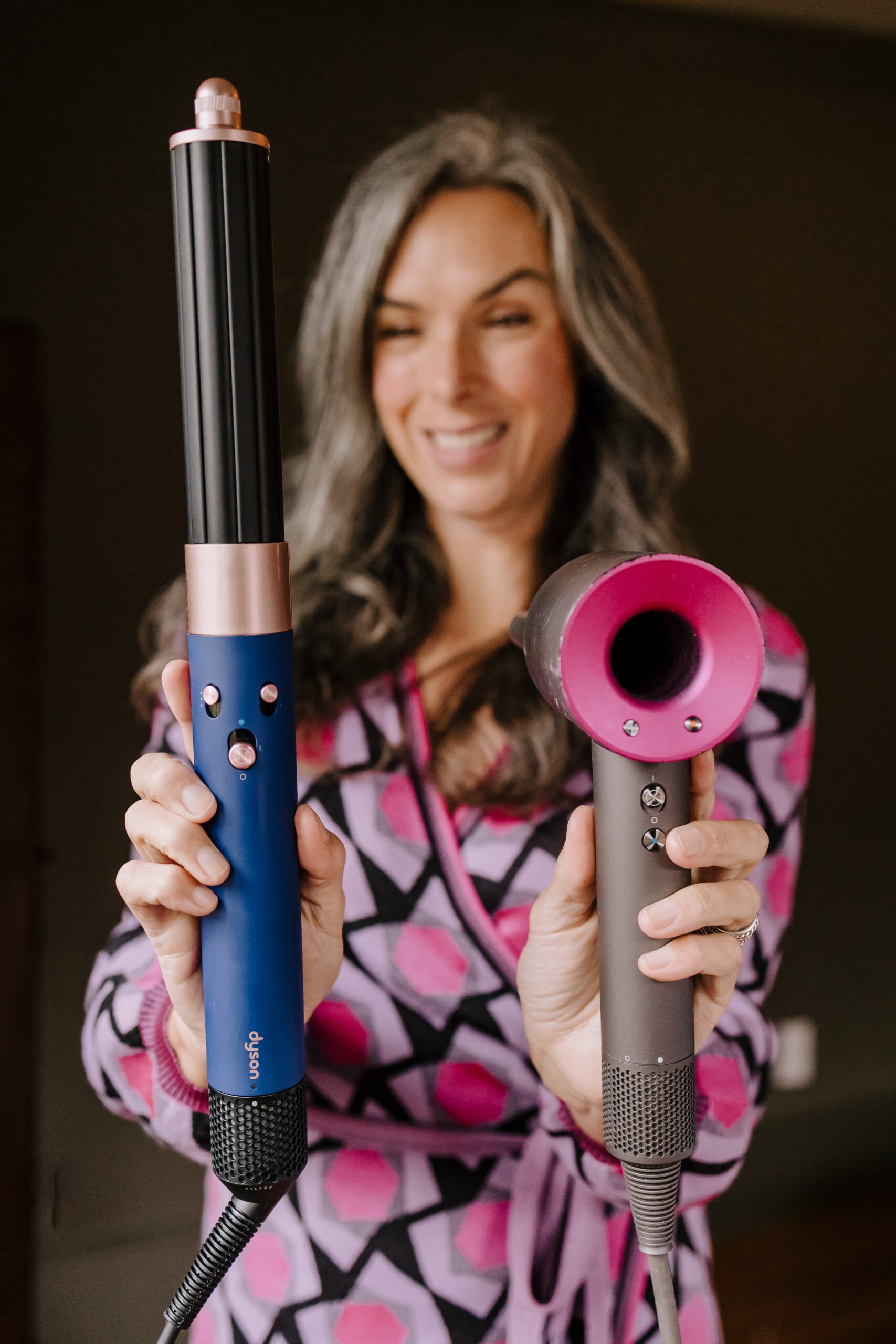 Lisa holds up the Dyson Hair Dryer and Airwrap to compare.