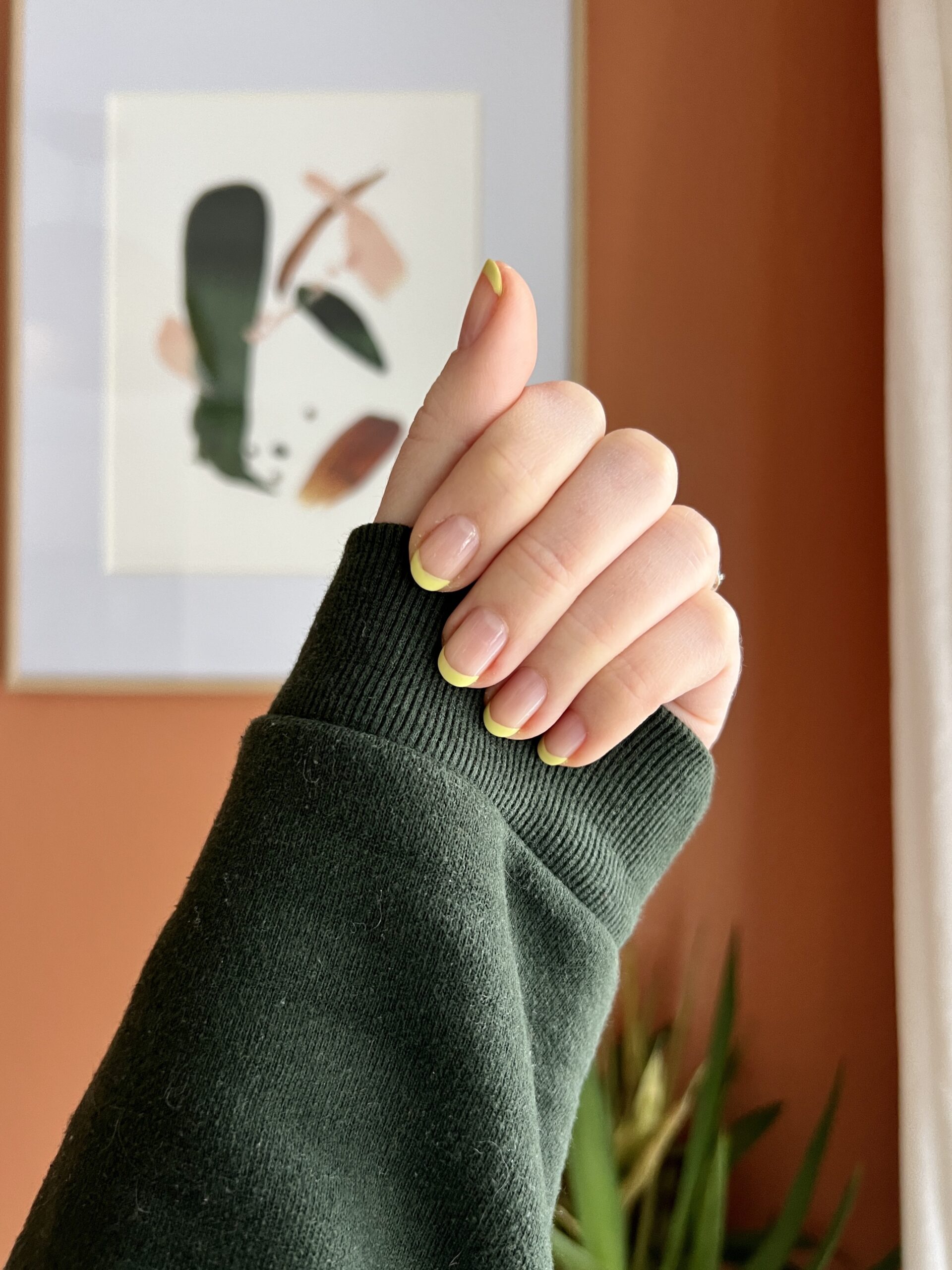A close up of a hand with green french manicure nails.