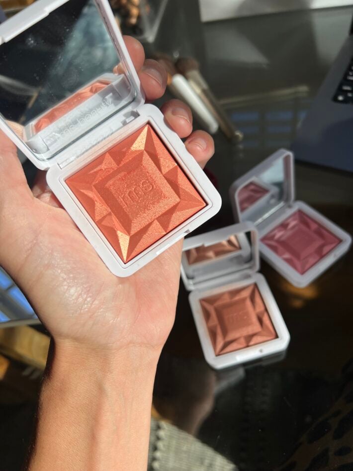 A hand holds up RMS “re” dimension hydra powder blush comes in 6 shades.