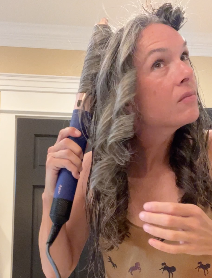 A woman styles her long gray hair with the Dyson Airwrap.