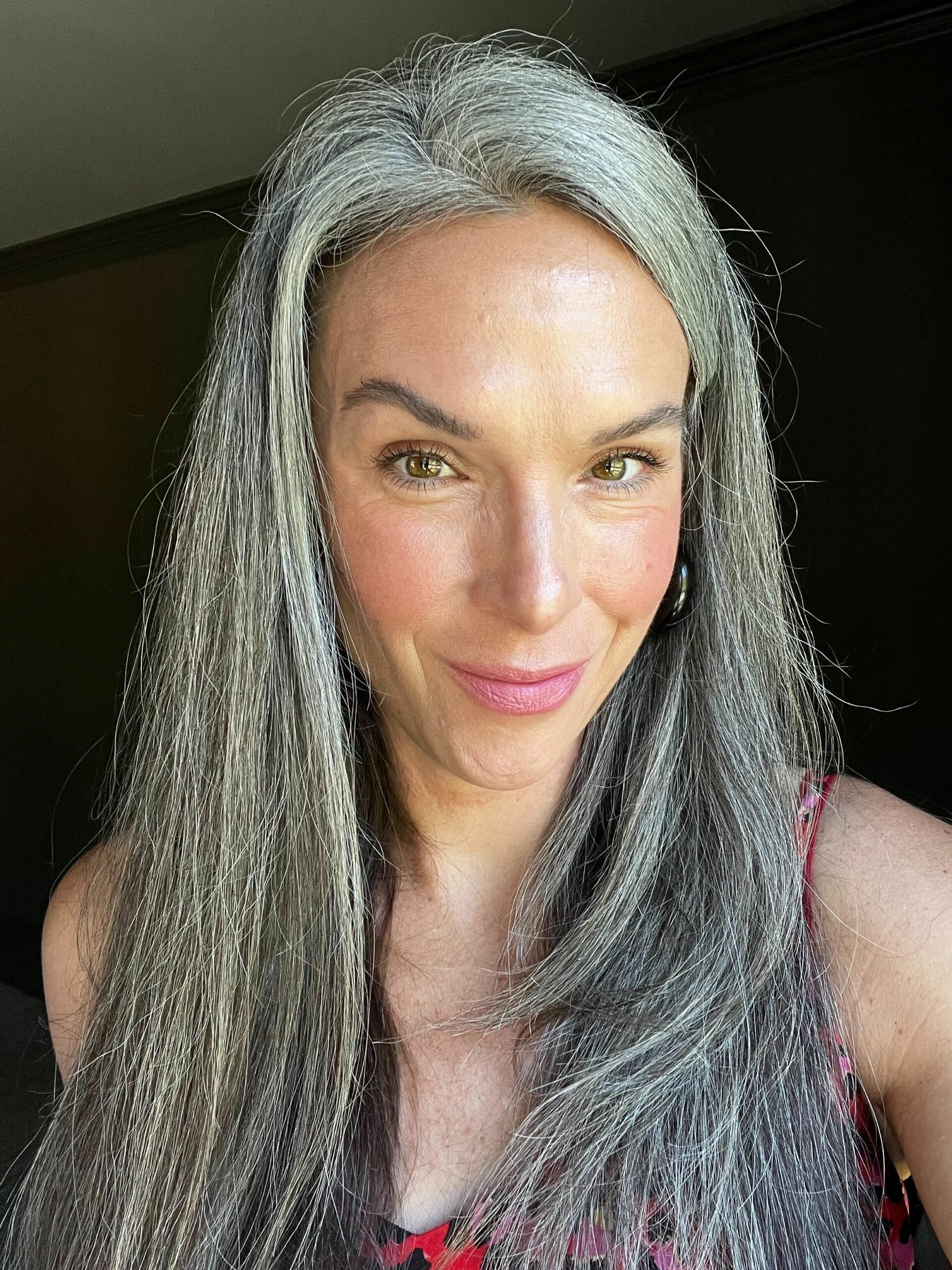A woman with long gray hair after it with the firm smoothing brush attachment by Dyson.