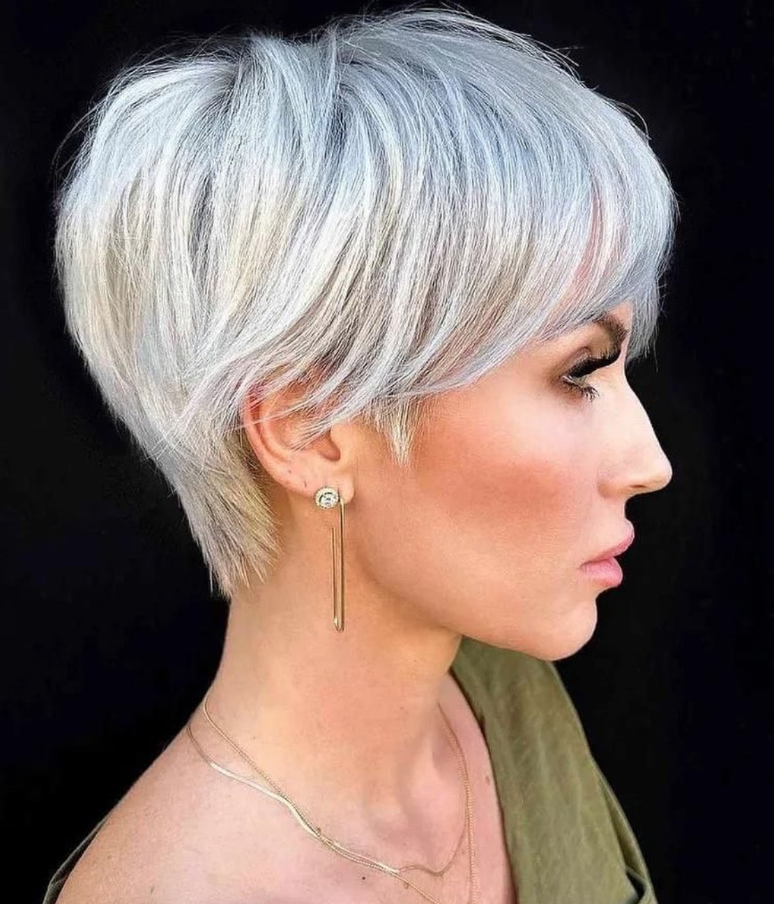 The side profile of a woman with long earrings and gray pixie cut. 