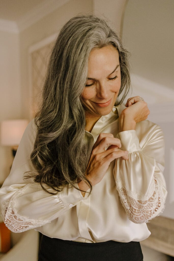 A woman with long wavy hair wearing LILYSILK's Armeria Lace Blouse in Lily White.