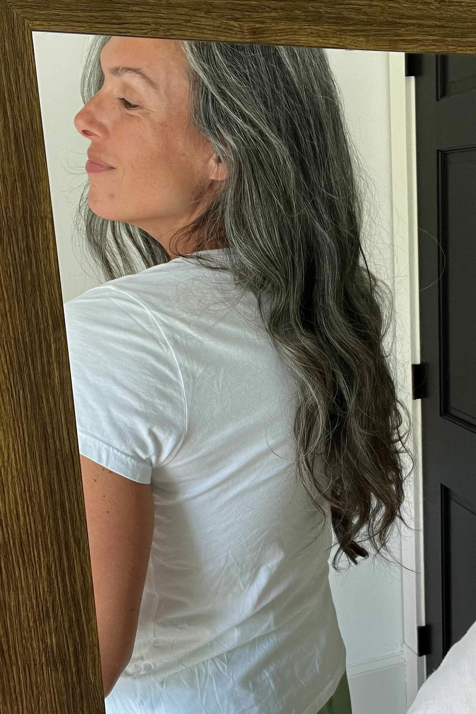 A woman with long gray hair wears a white t-shirt.