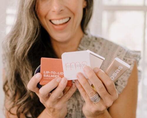 A woman holds up a collection of beauty products in her hands.