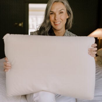 A woman sits on her bed holding up a pillow in her arms.