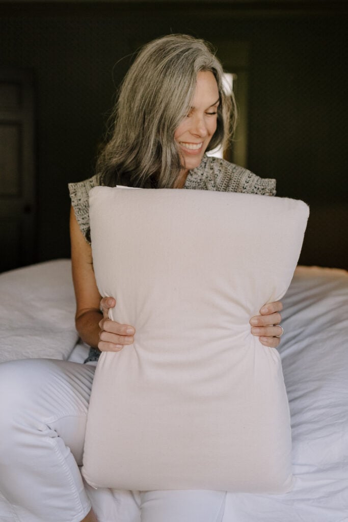 A woman holds up a pillow in her arms.