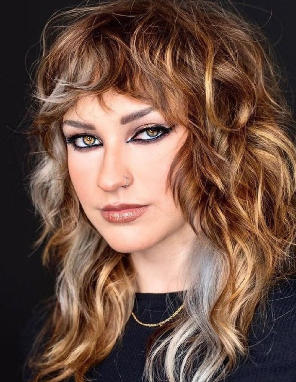A woman with a multi-colored hair and dark eyeliner looks off to the side.