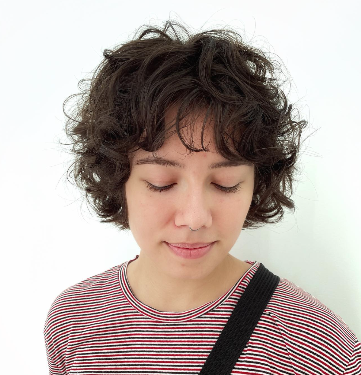 A woman with a nose ring and curly brown hair looking down. 