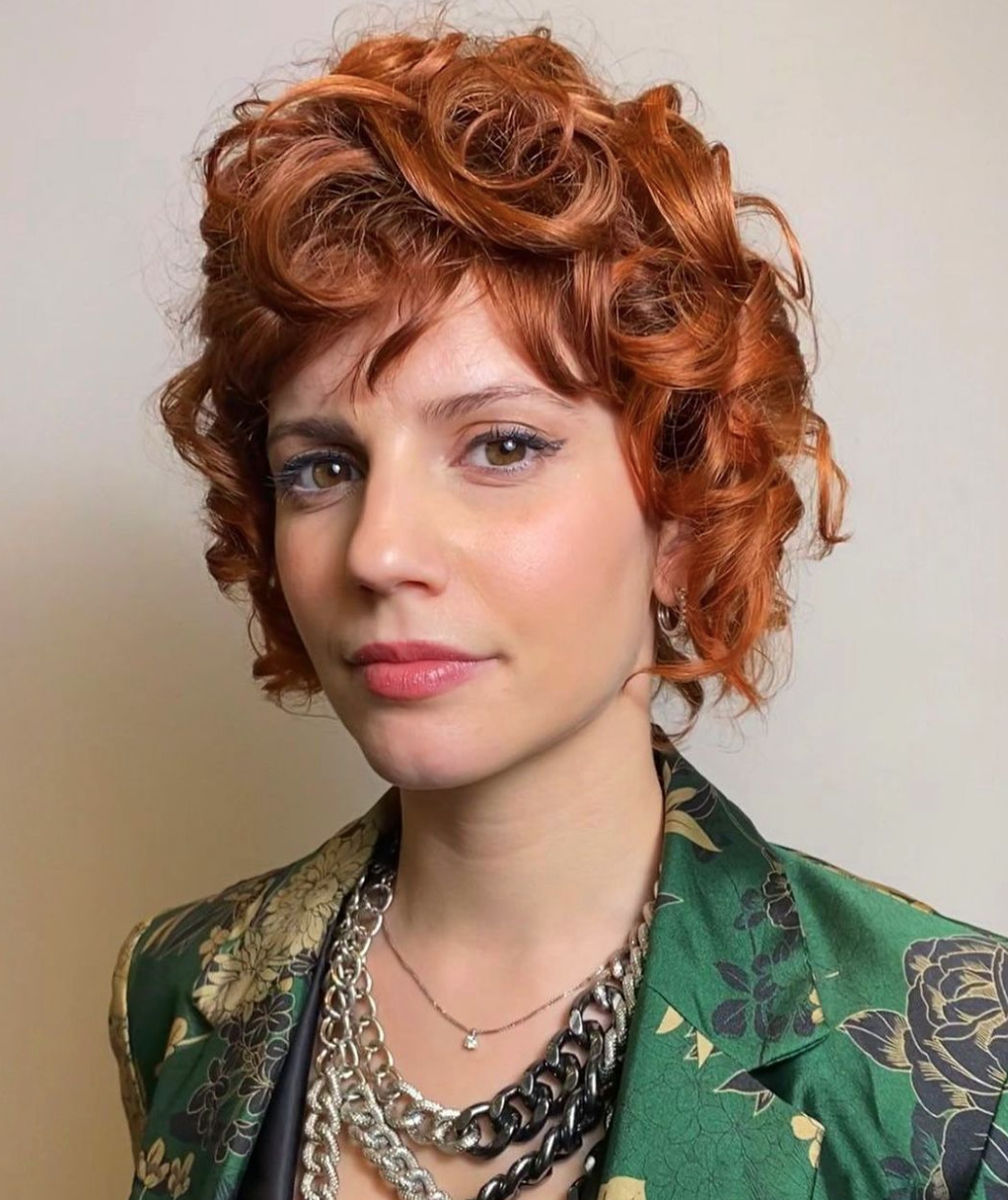 A woman with curly red hair looks straight onward. 