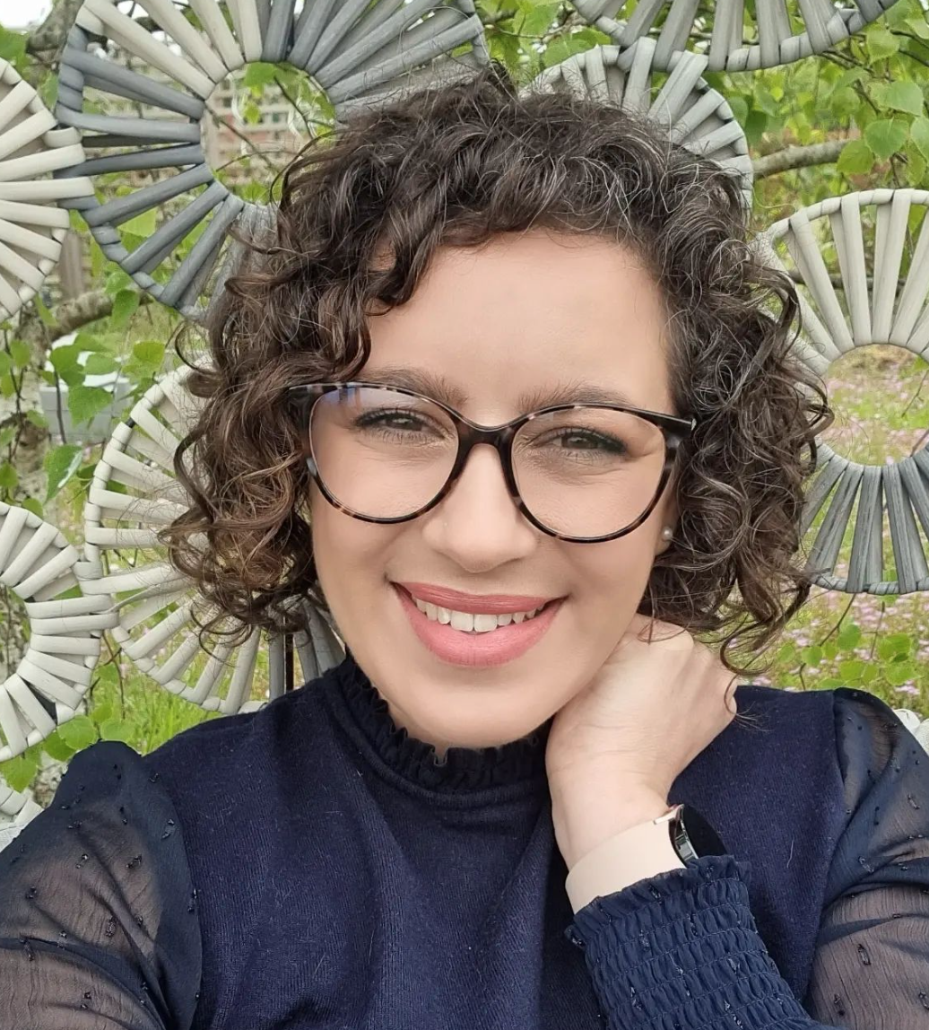 A curly brown haired woman in glasses smiles.