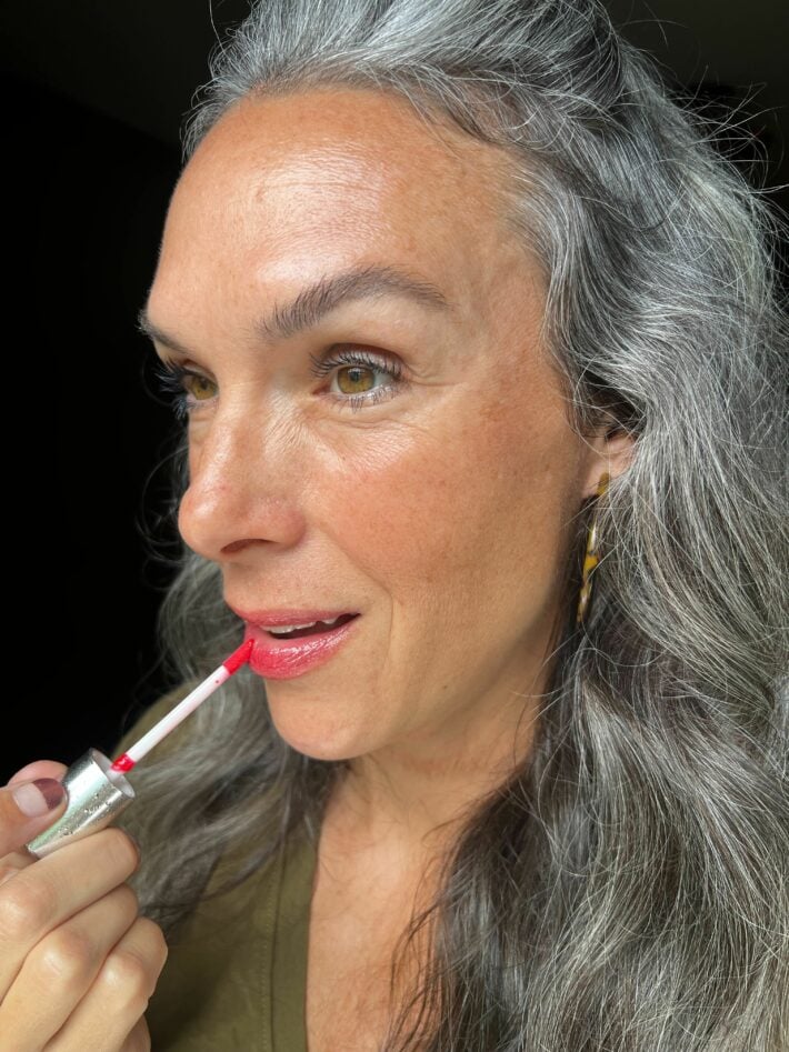 A woman applying Fitglow lip serum to her lips.