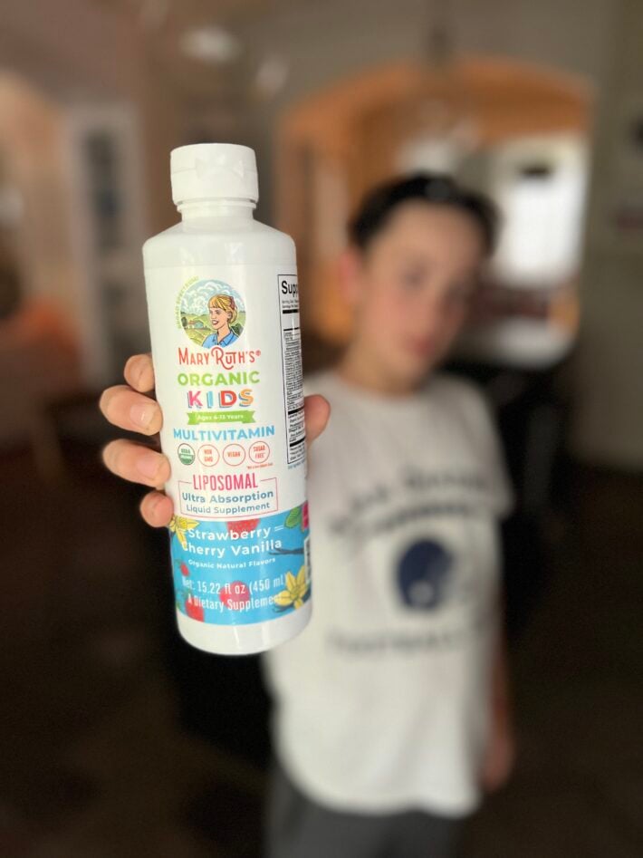 A boy holds up a bottle of MaryRuth Organics liquid vitamins.