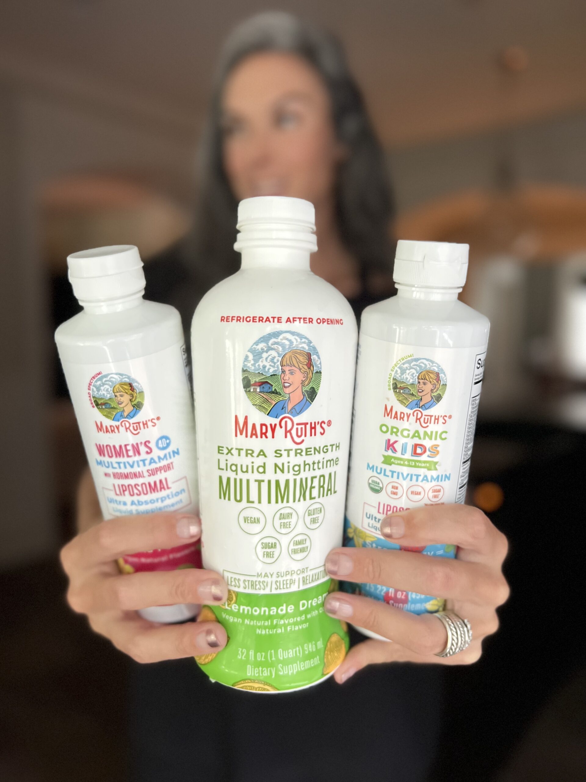A woman holds up three bottle of liquid vitamins from MaryRuth Organics.