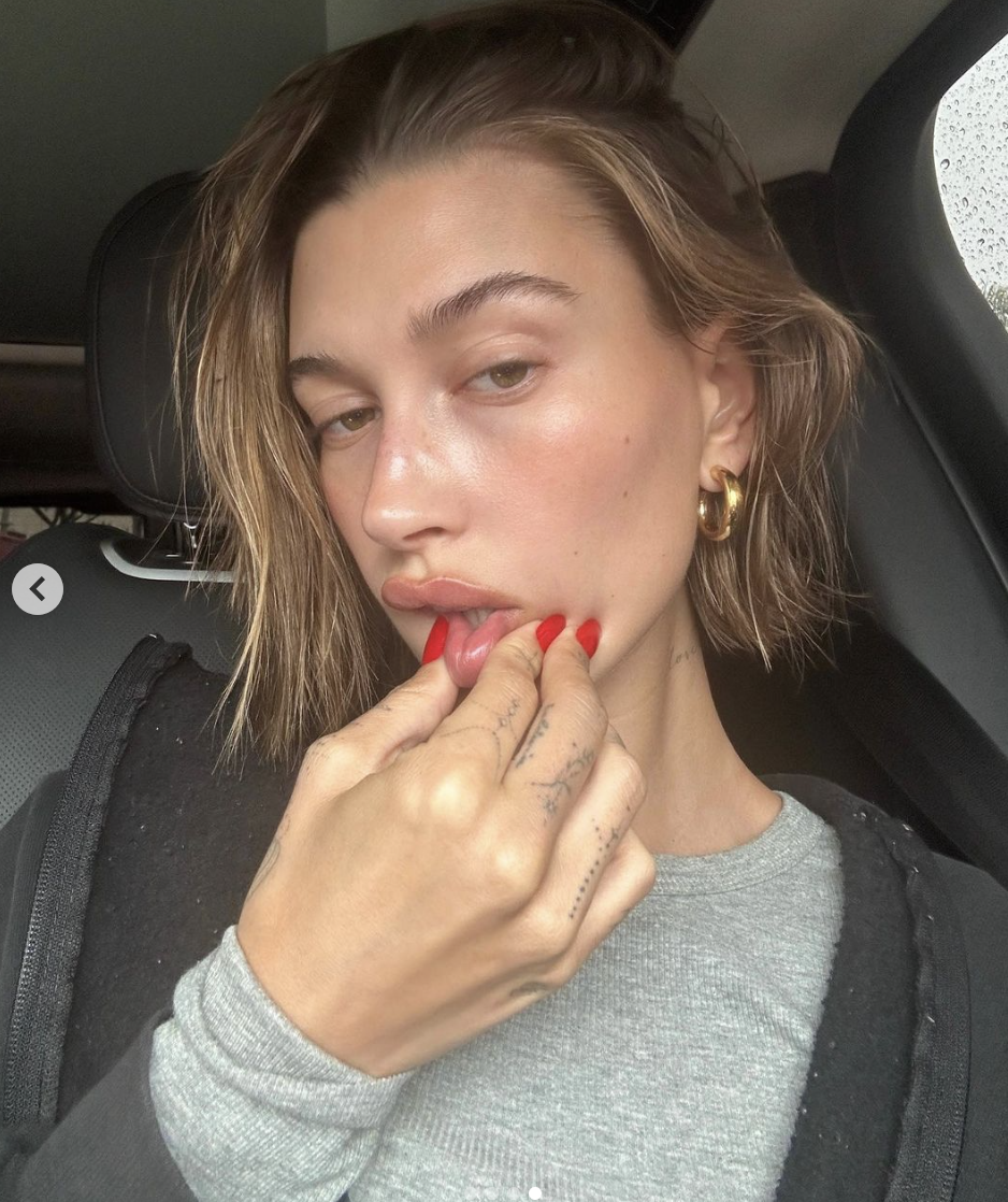 Hailey Bieber shows off her cherry red nails with a car selfie.