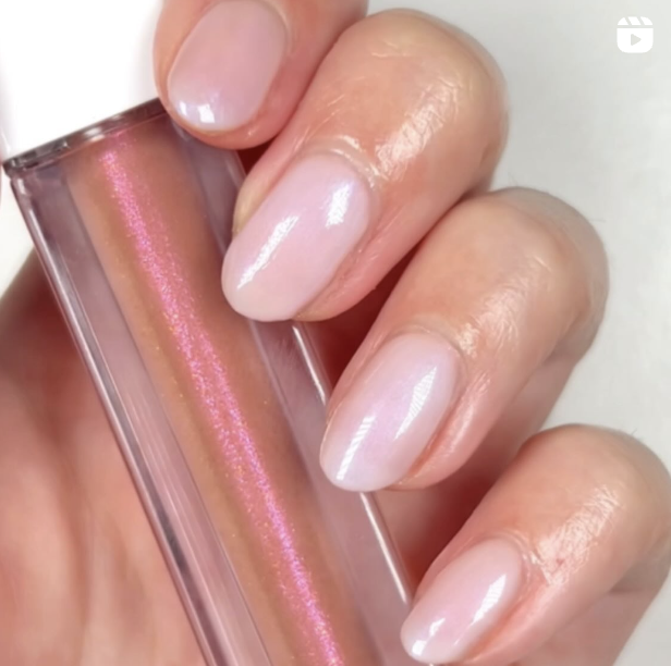 A woman shows off her sheer rose nail polish while holding lipgloss.
