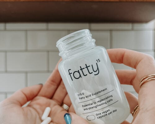 A hand holds a bottle of Fatty15 supplements up.