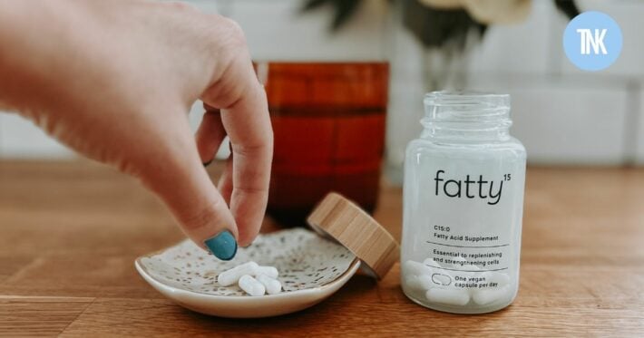 A close up of a bottle of fatty15 and capsules on a small bowl.