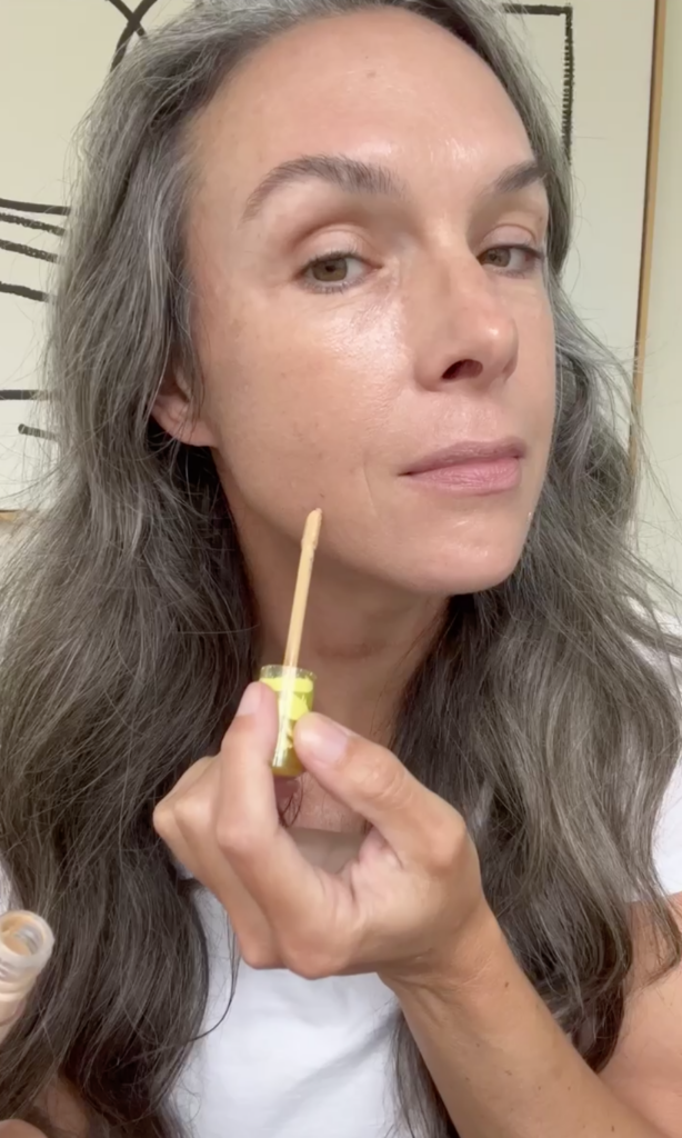 A close up of a woman's face as she uses Kosas Revealer Concealer.