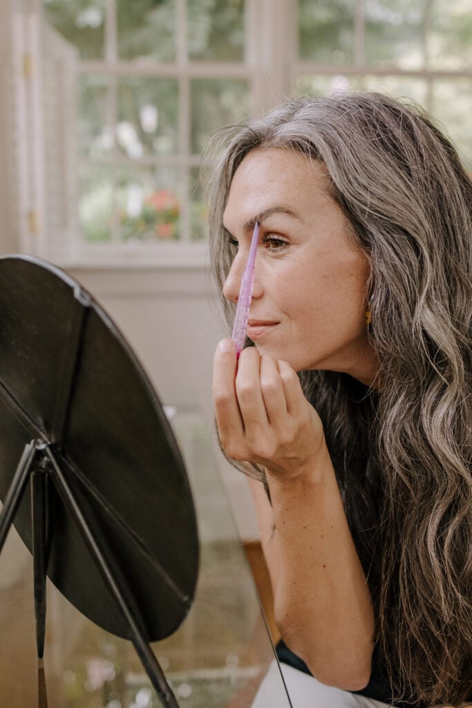 A woman applying Kosas brow pop while looking in the mirror.