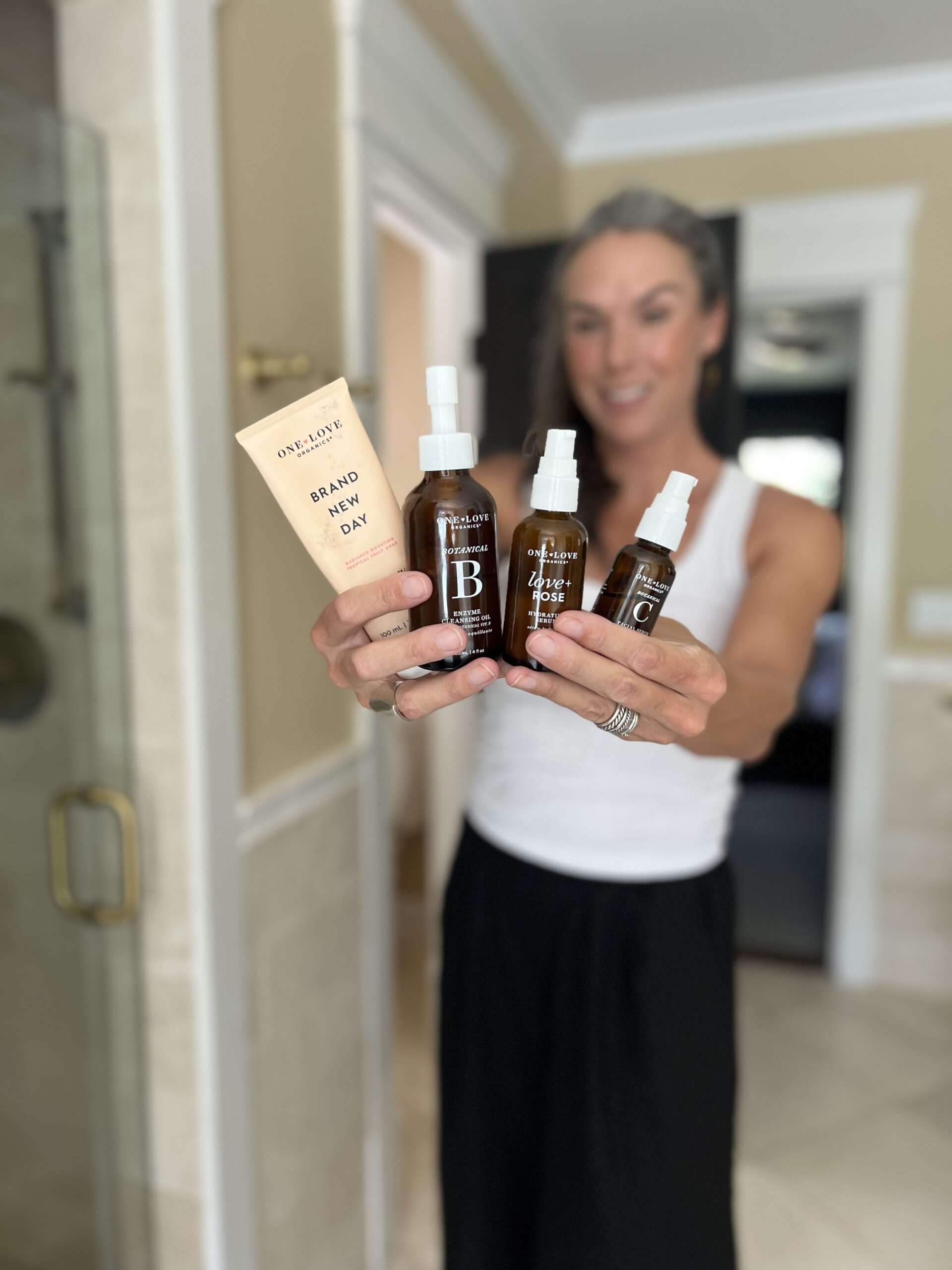 A woman holds up a collection of products from One Love Organics.