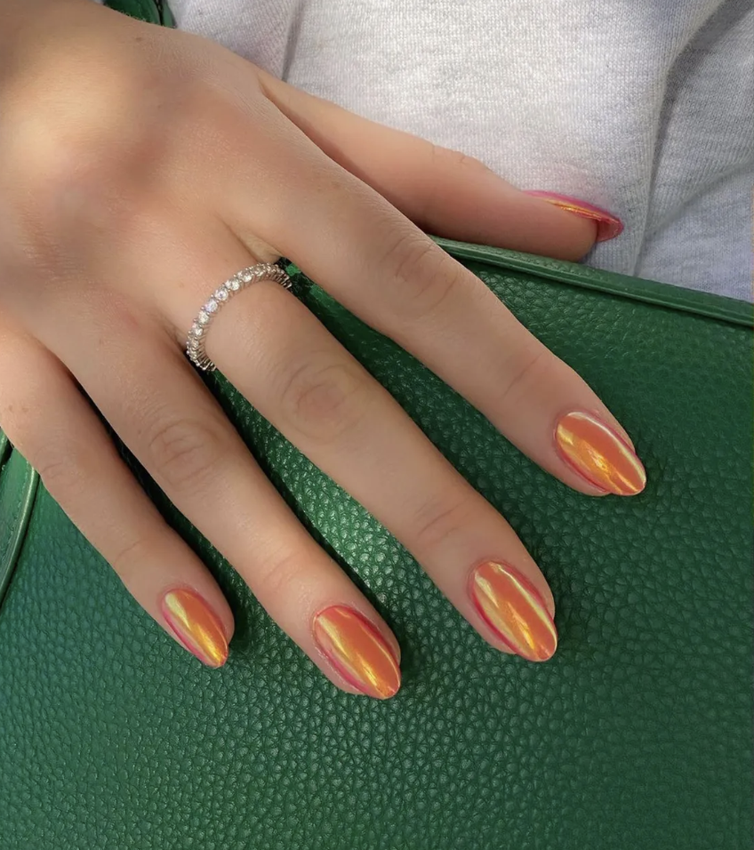 A woman's hand rests on a green purse, with glazed neon orange nail polish.