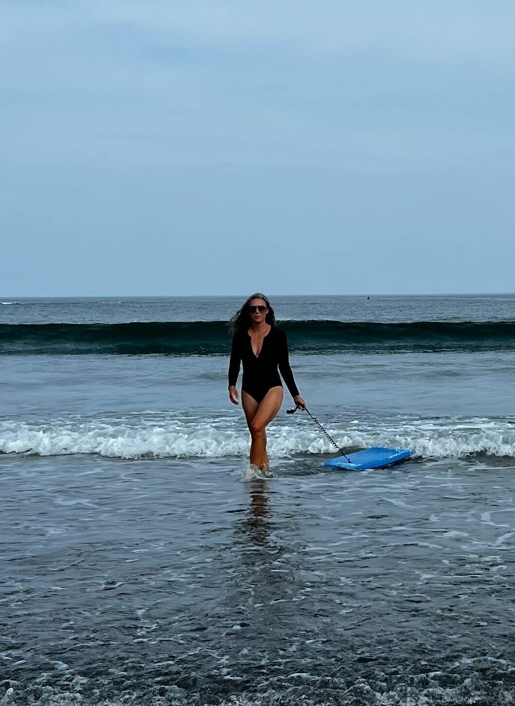 A woman on the beach in a black swimsuit with long sleeves. 
