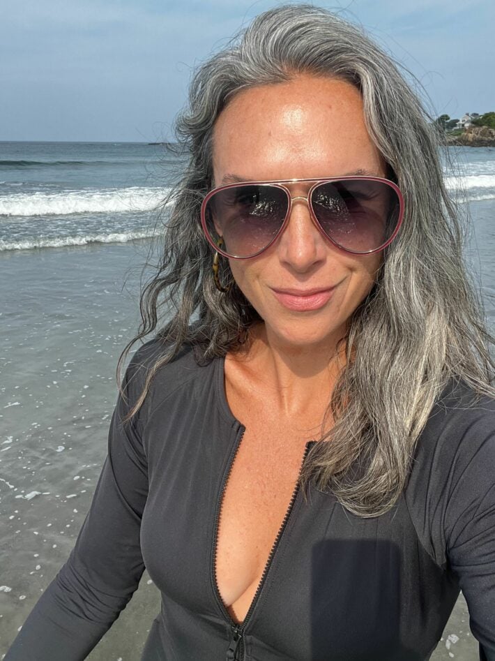 A woman in sunglasses and a long sleeved black swimsuit.