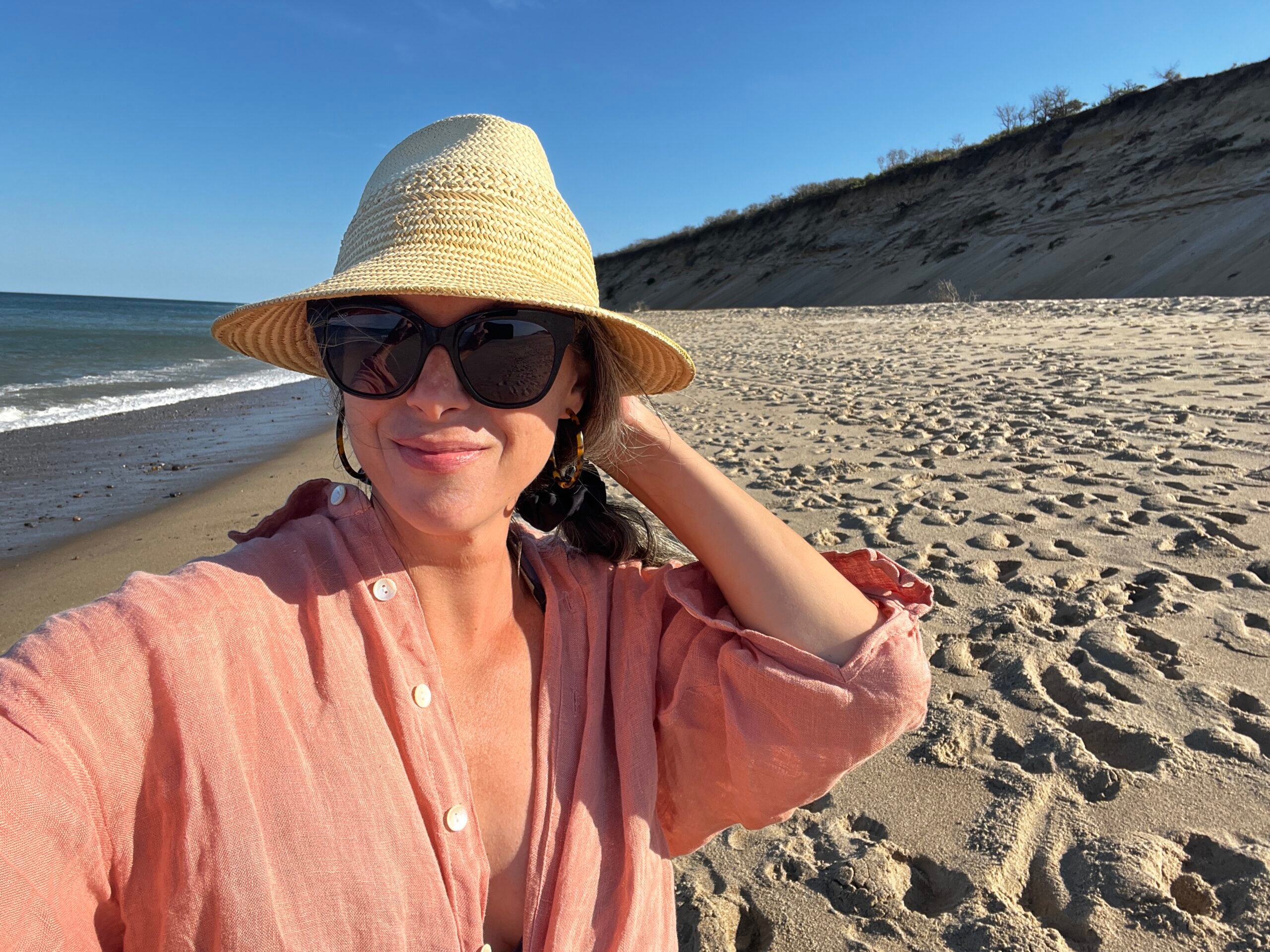A woman walks on the beach wearing a sun hat.