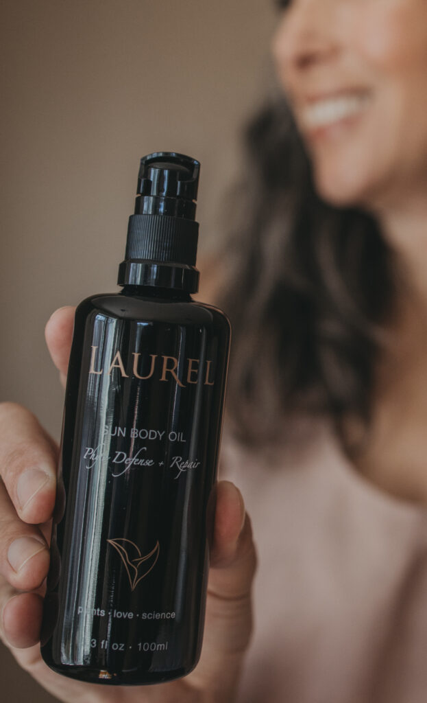 A woman holds up a bottle of Laurel Sun Body Oil.
