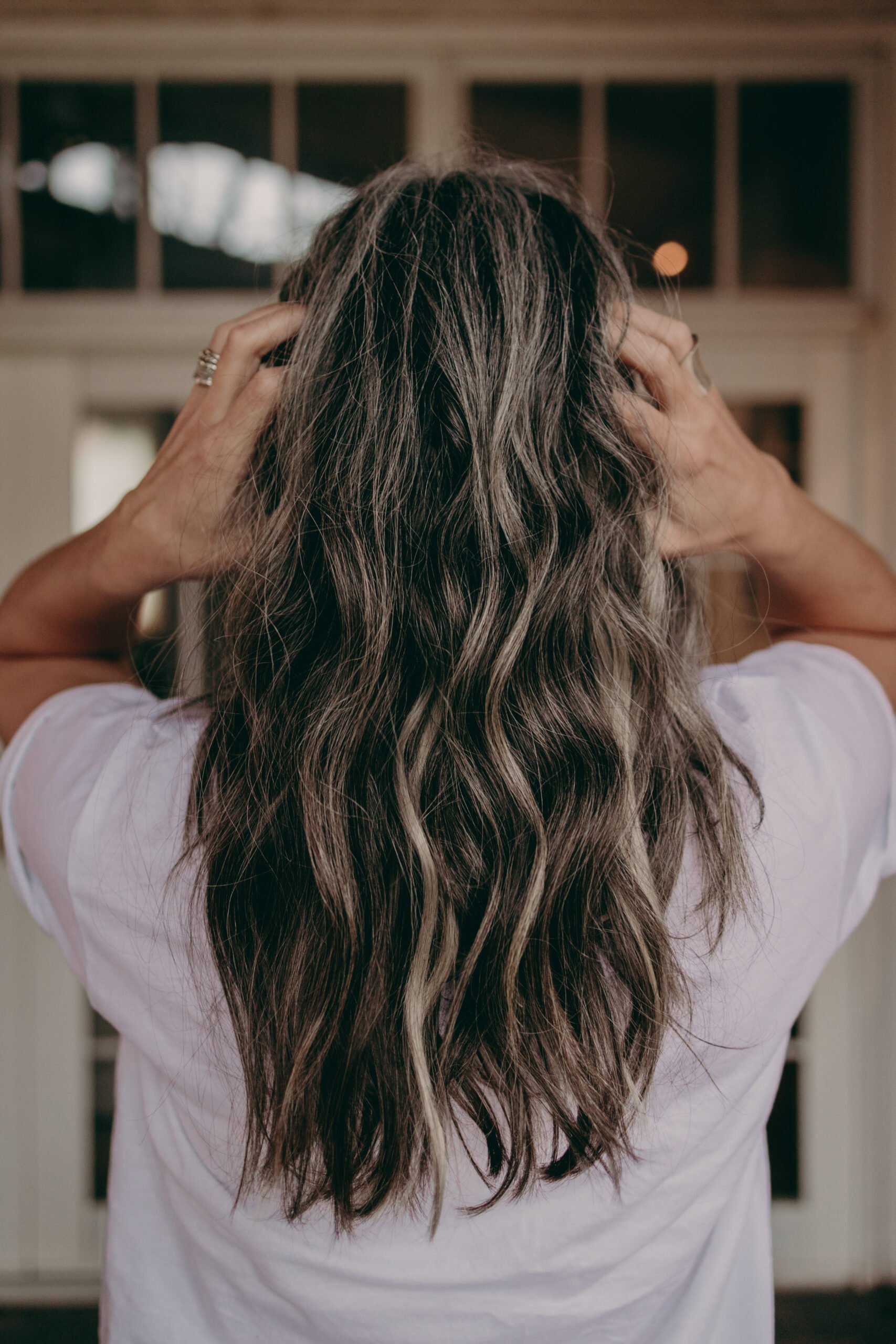 A back of a woman's head who has long wavy gray hair. 