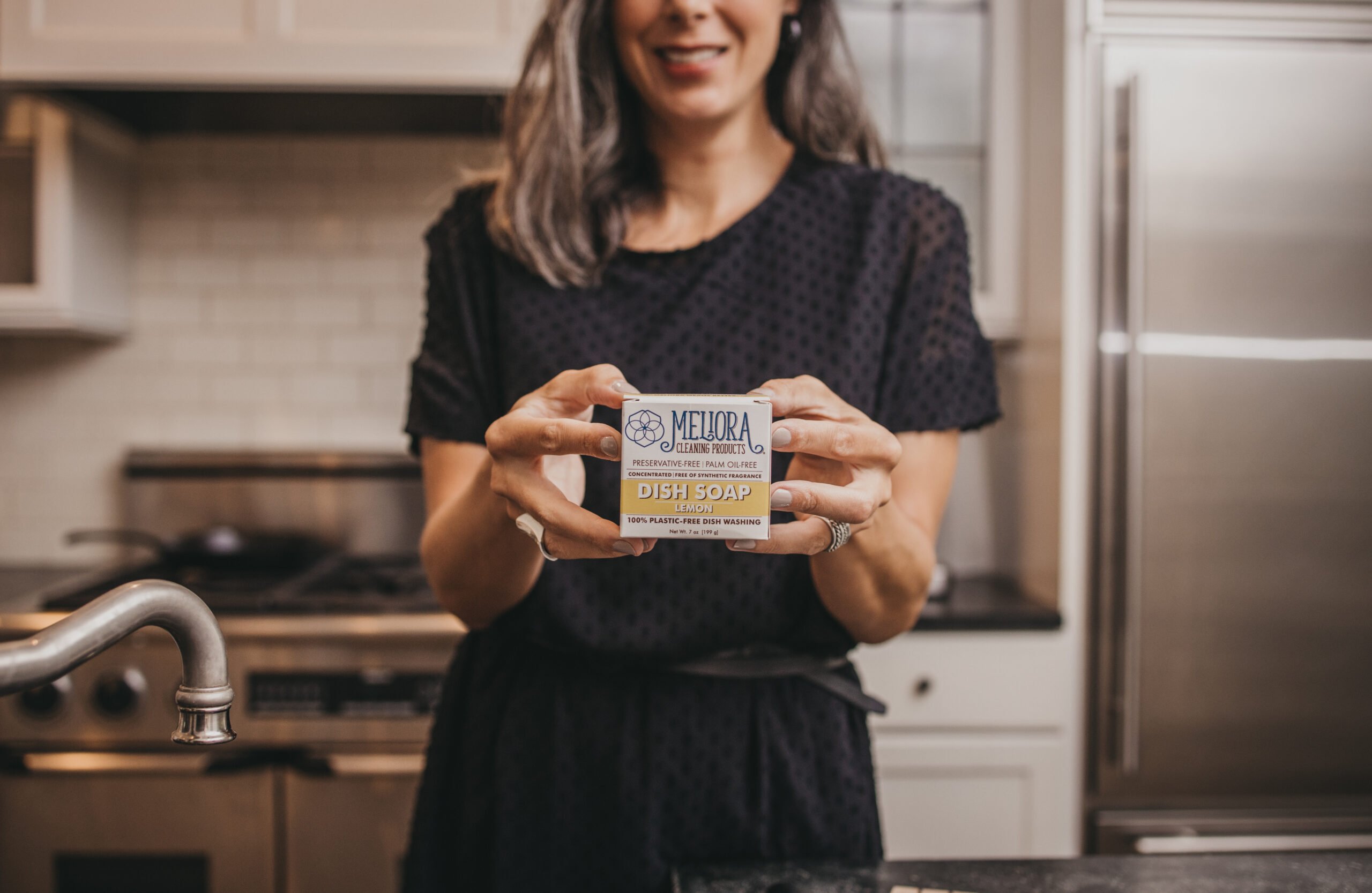A woman holds up a box of dish soap.