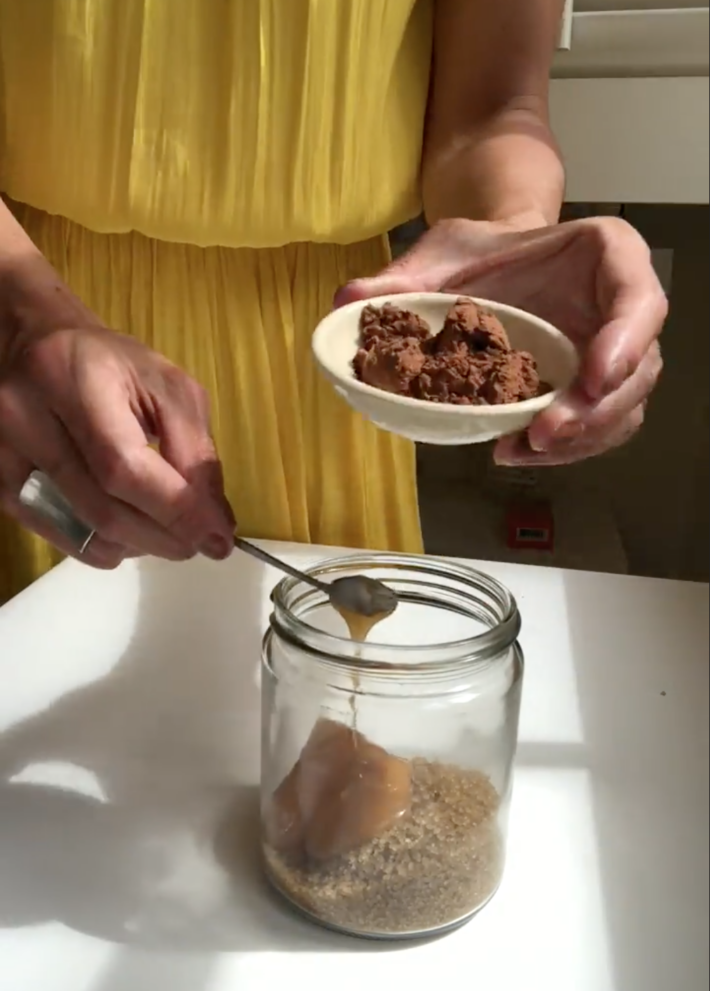 A woman mixes honey into a body polish recipe.