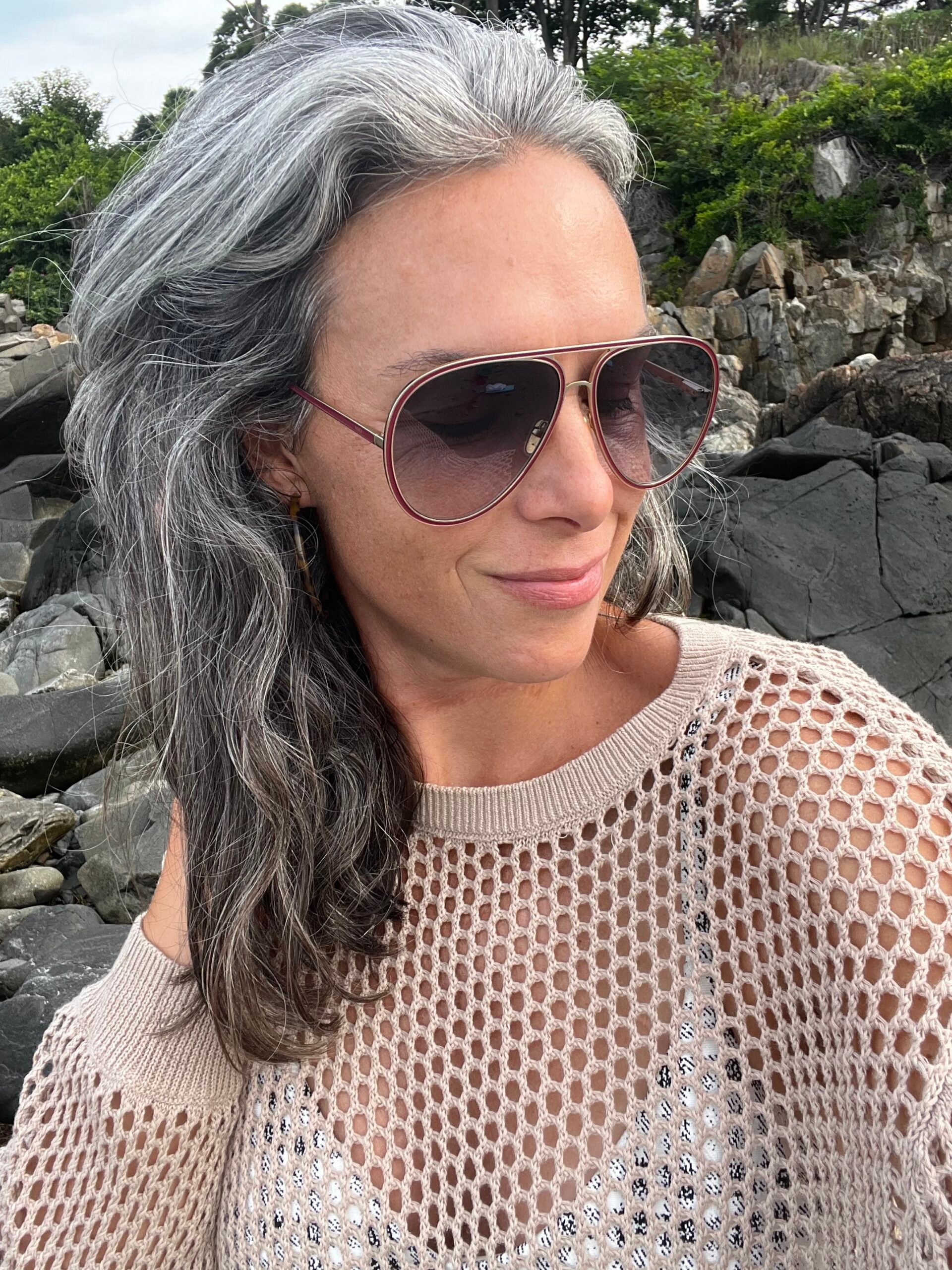 A woman with wavy gray hair sits on the beach.