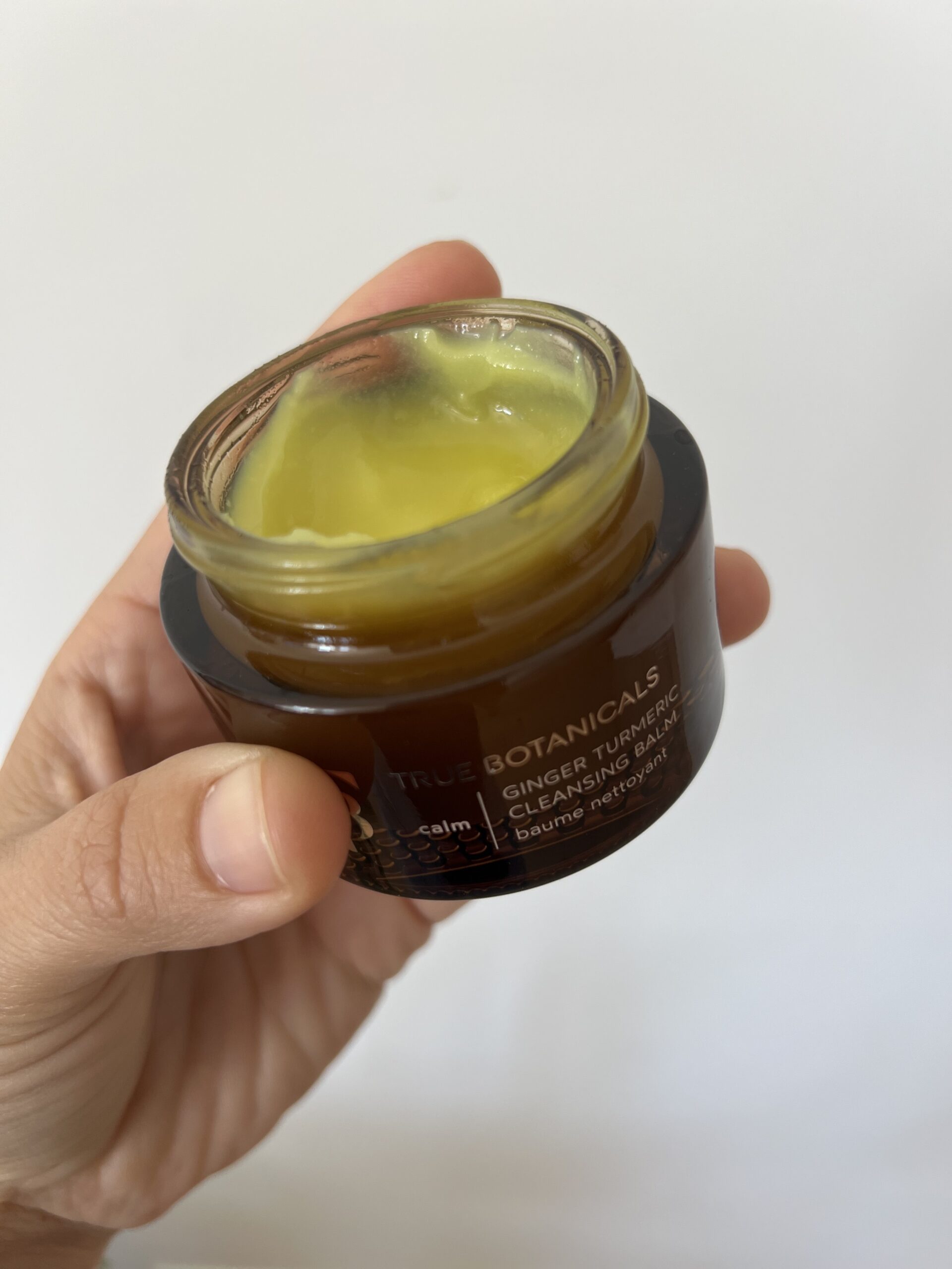 A hand holds up True Botanicals ginger turmeric cleansing balm.
