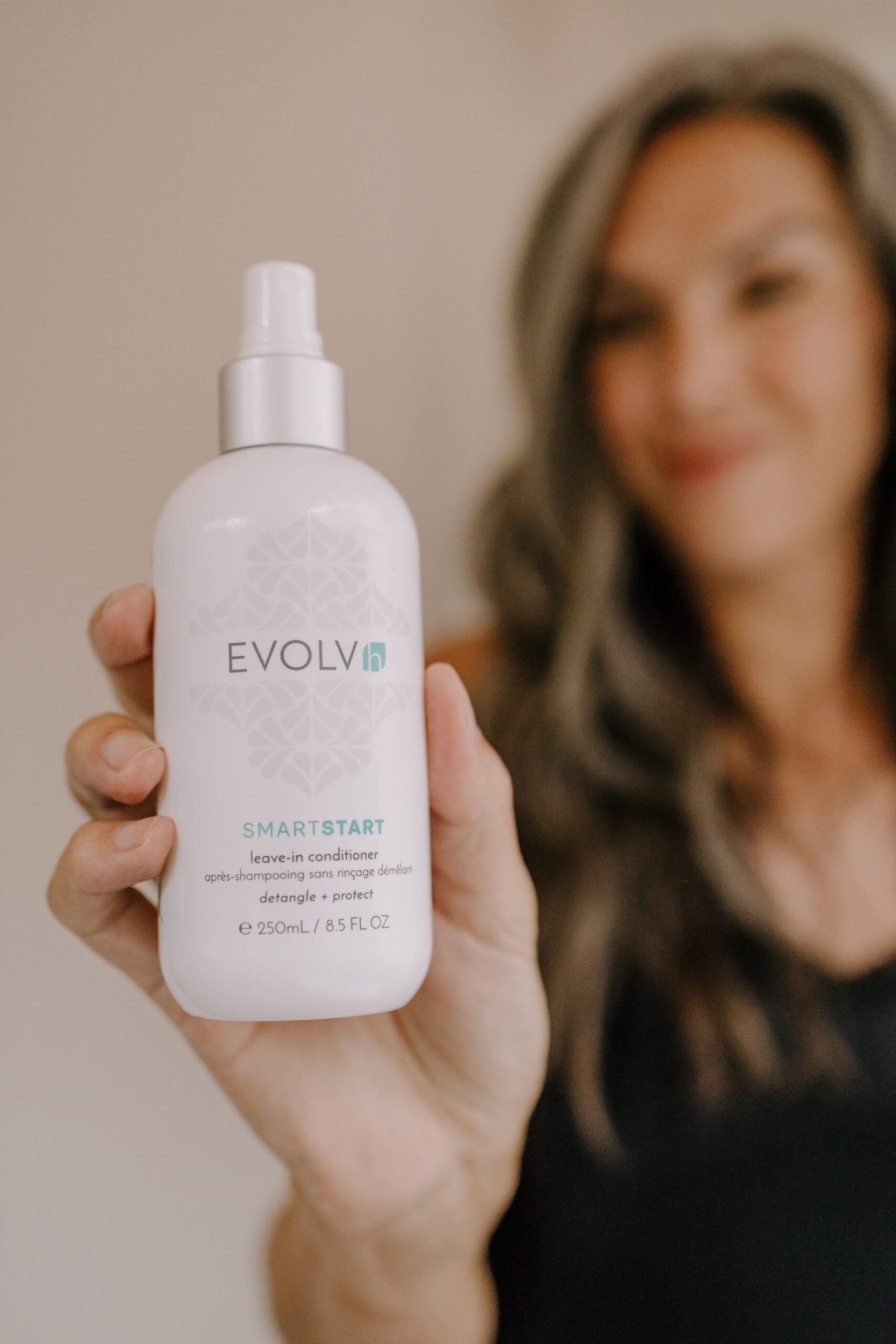 Woman holding up bottle of Evolvh Smart Start Leave in Conditioner