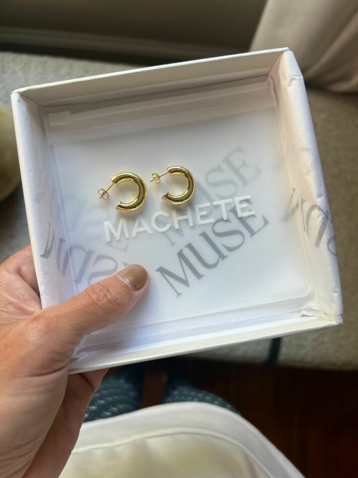 A hand holding a box of Machete Muse earrings. 