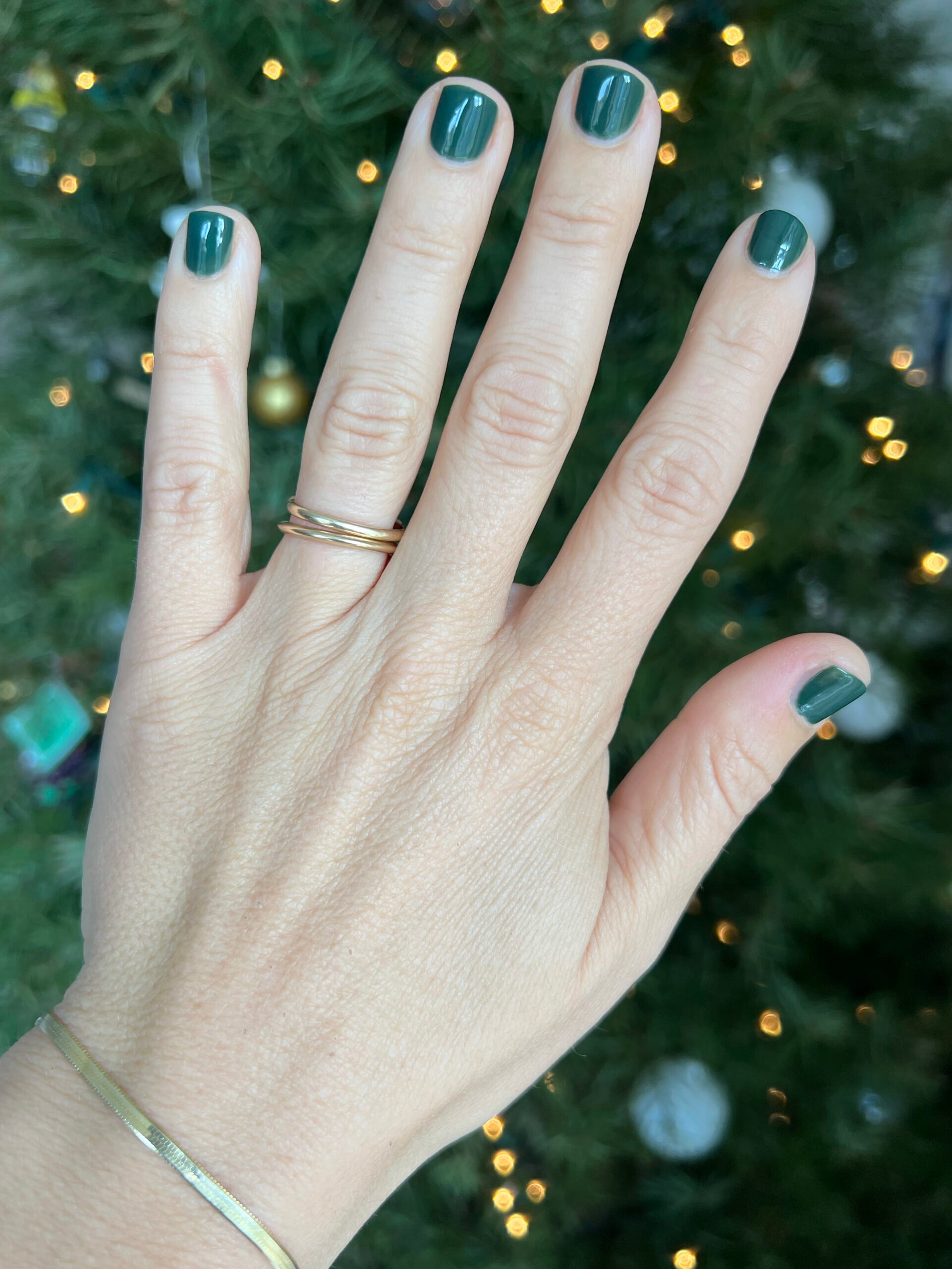 A close up of a hand with dark green nail polish. 