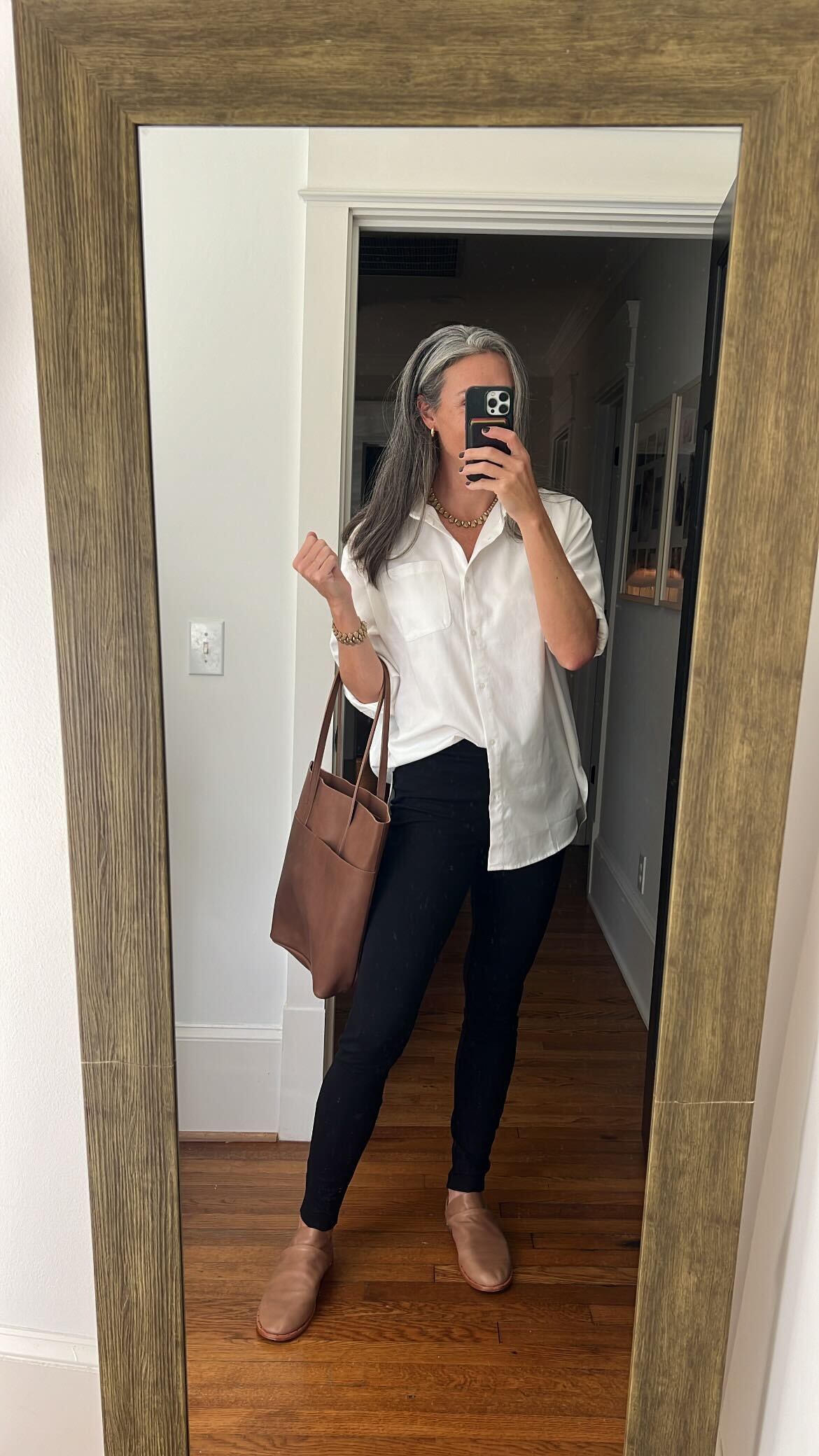 A woman in a white button down shirt and black pants taking a selfie. 