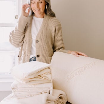 A woman smiles while looking down at Savvy Rest organic bedding.